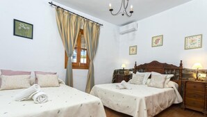 Una habitación con dos camas, un cabecero de madera, una mesita de noche con lámpara y una ventana con cortinas.