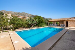 Une piscine rectangulaire à l’eau d’un bleu limpide, entourée d’une terrasse en pierre. On y trouve des chaises longues et une pergola surmontée d’un toit en tuiles.