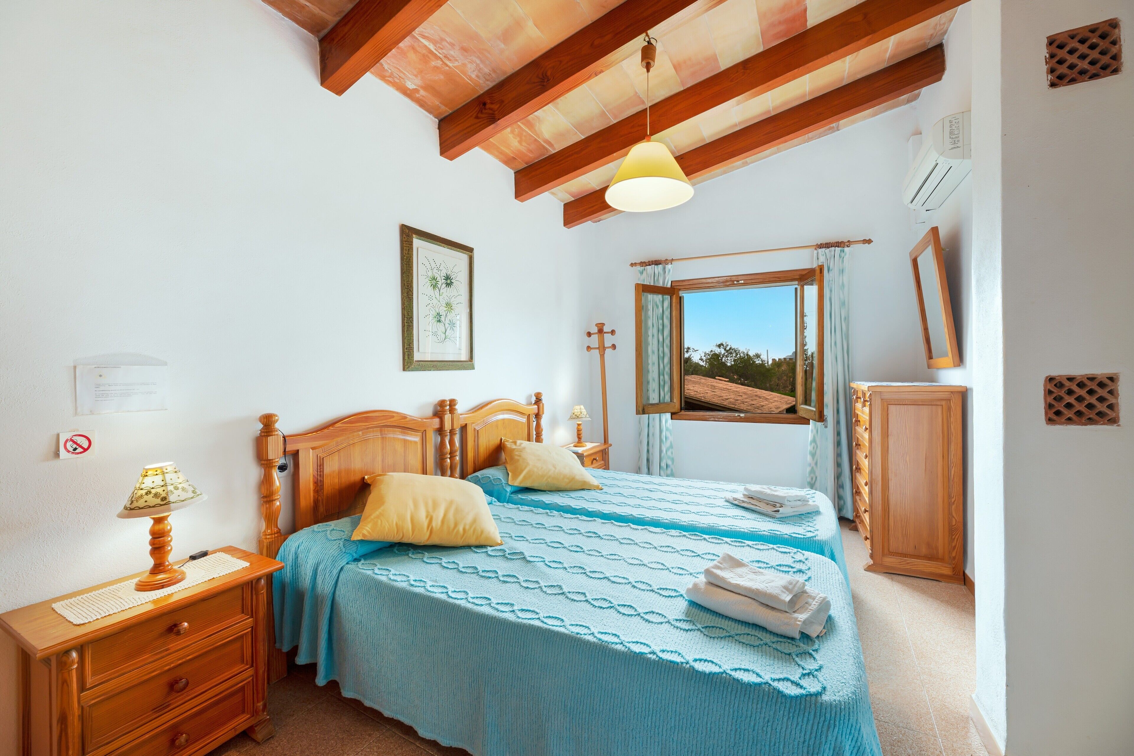 A bedroom with a wooden bed, a nightstand, a lamp, a window with a view, and a wooden wardrobe.