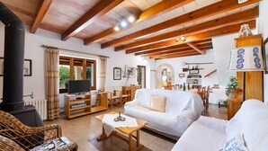 A cozy living room with a fireplace, white sofas, wooden furniture, and a television. - Holiday Home "Can Noble den Suau" with Pool, Hot Tub, Terraces & Garden (Pollensa)