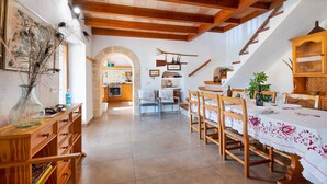 A dining area with wooden furniture, a staircase, and a kitchen in the background. - Holiday Home "Can Noble den Suau" with Pool, Hot Tub, Terraces & Garden (Pollensa)
