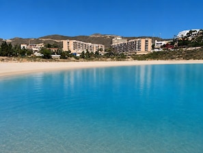 Ein klares, blaues Schwimmbecken mit Sandstrand und Gebäuden im Hintergrund.