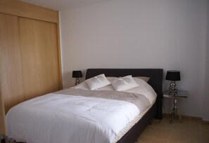 Ein Schlafzimmer mit einem Bett, zwei Nachttischlampen, einem Holzschrank und einem Fliesenboden.