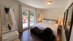 Habitación de hotel con una cama grande, zona de estar, puerta de vidrio que da a un área exterior con piscina y sillas, e iluminación en el techo.
