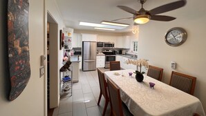 Una cocina moderna con armarios blancos, un refrigerador de acero inoxidable y un comedor con una mesa lista para dos.