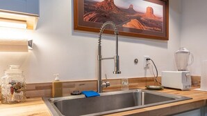 Een keuken met een roestvrijstalen spoelbak, een lijst met een foto van Monument Valley en een broodrooster op het aanrecht.