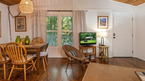 Een houten eettafel met stoelen, een televisie en een rieten fauteuil.