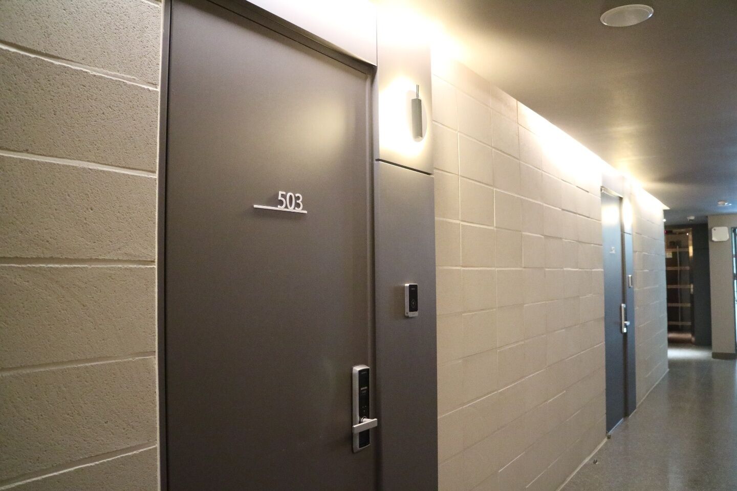 Un pasillo con una puerta que lleva la etiqueta '503' y una lámpara fijada a la pared.