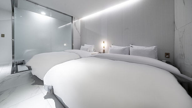 A modern hotel room with a large bed, a glass shower enclosure, and a wall-mounted light fixture.