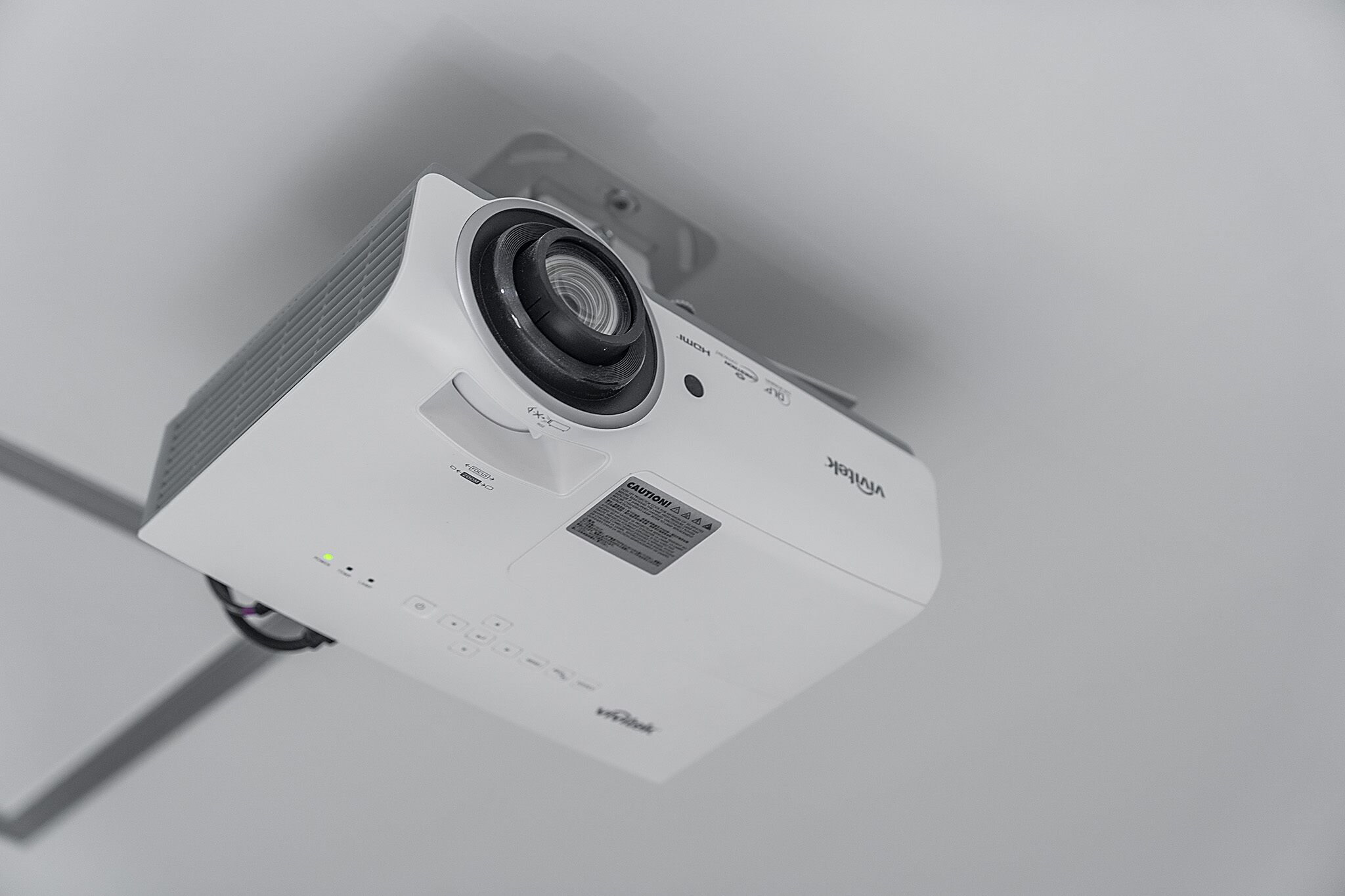 A white projector with a lens and ventilation grilles, mounted on a wall.