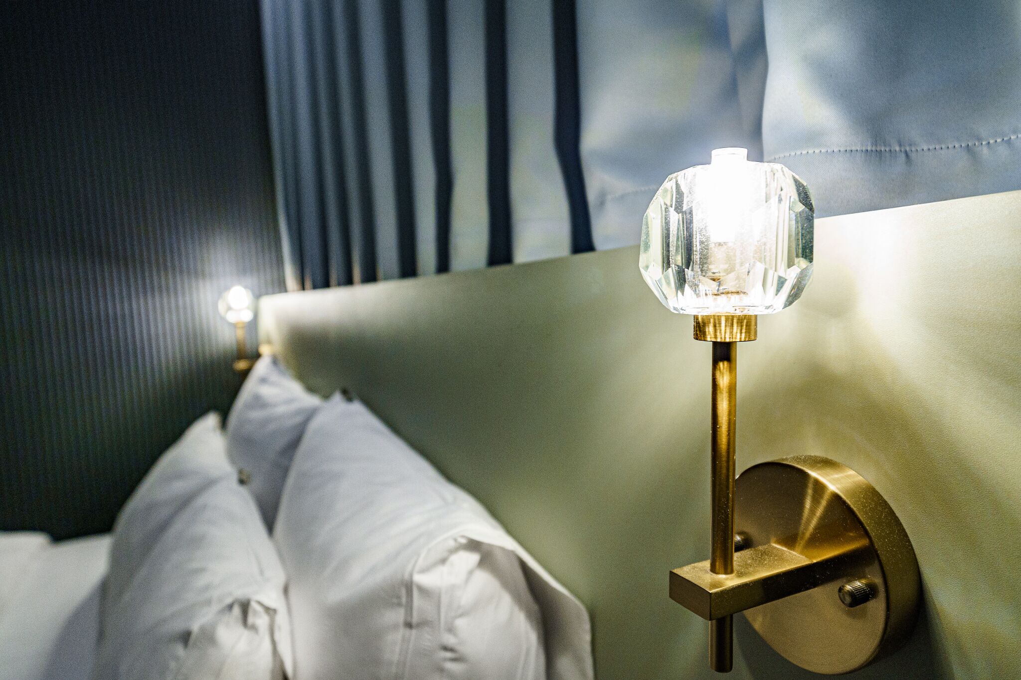 A bed with white linens and a bedside lamp with a crystal shade.