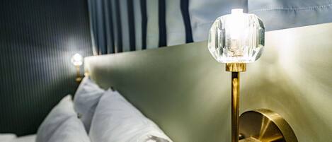 A bed with white linens and a bedside lamp with a crystal shade.