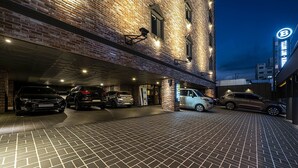 A parking garage with multiple cars parked under a building with exposed brick walls and a sign with a 'B' logo.