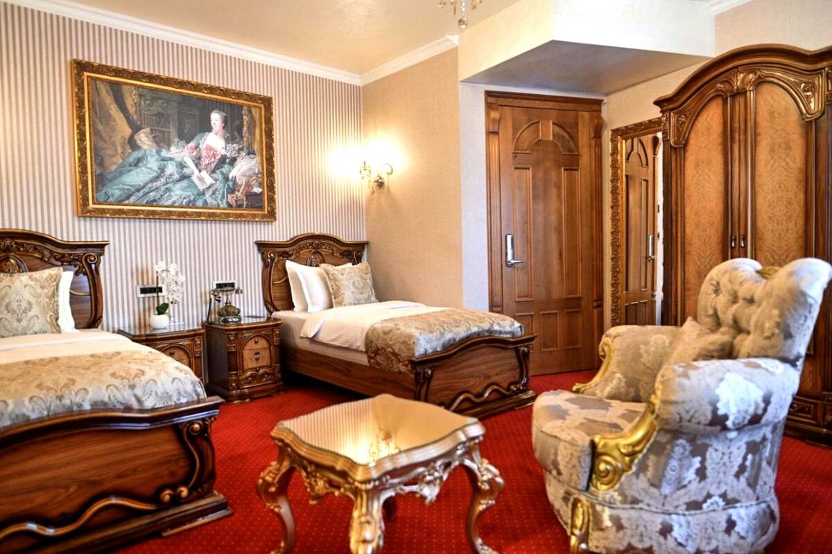 A room with two beds, a wooden wardrobe, a chair, and a painting on the wall.