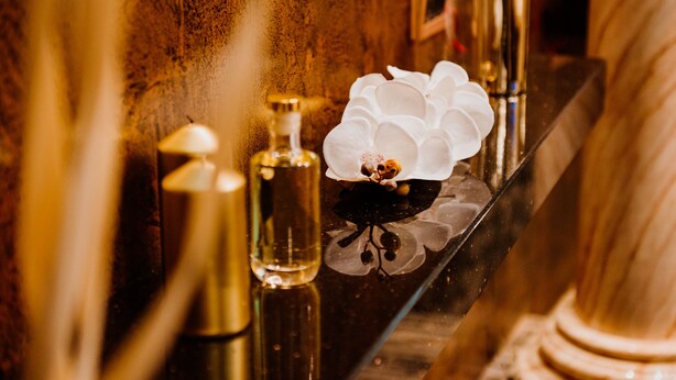 A bathroom vanity with a mirror, a white orchid, and two gold-colored bottles. - Prezident Palace Belgrade - Rooftop Pool & Spa Hotel (Belgrade)