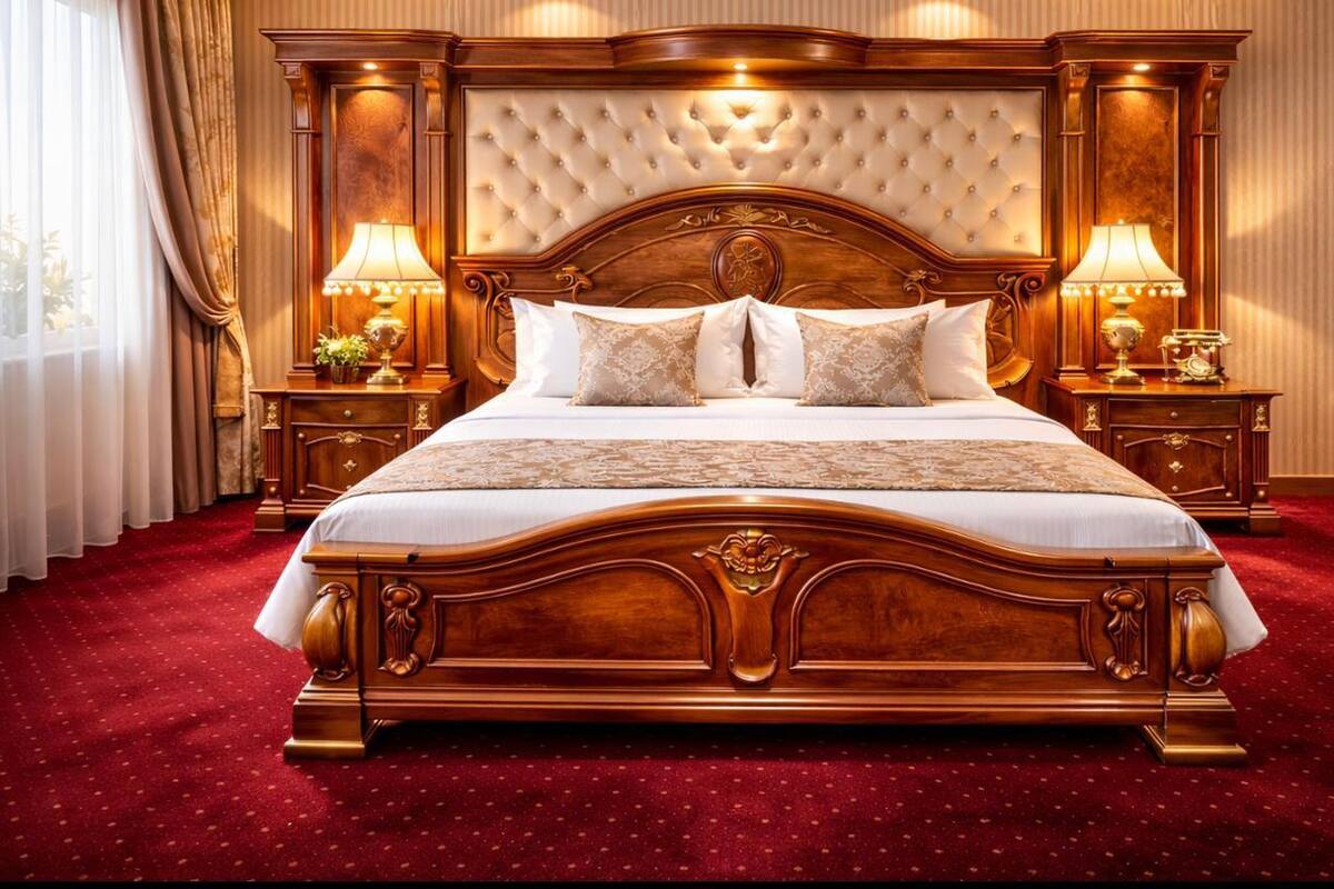 A large, ornate bed with a tufted headboard, two bedside tables with lamps, and a red carpeted floor.