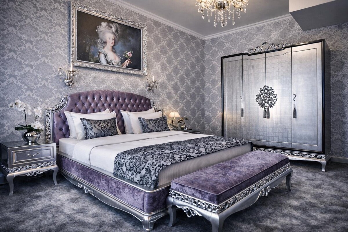 A bedroom with a large bed, a wardrobe, a chandelier, and a framed painting on the wall.