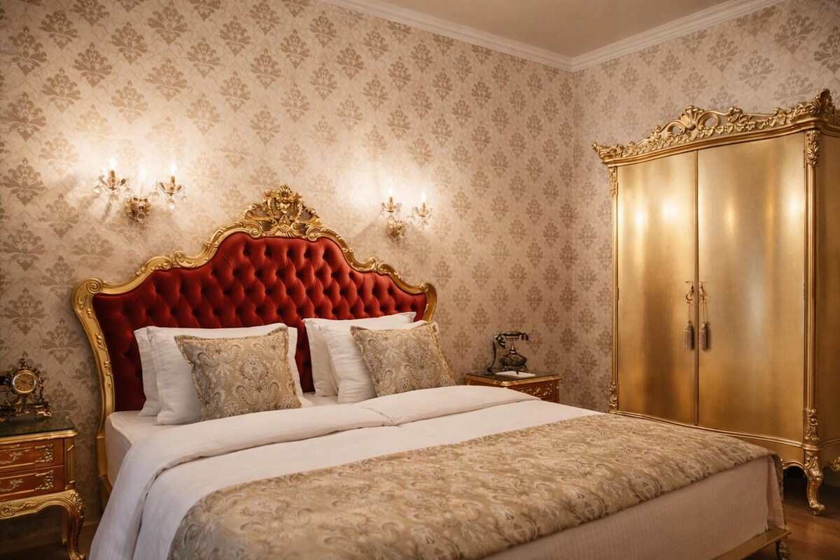 A bedroom with a tufted red headboard, a gold wardrobe, and patterned wallpaper.