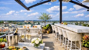 A rooftop terrace with a bar, seating, a champagne bucket, glasses, and a flower arrangement. - Prezident Palace Belgrade - Rooftop Pool & Spa Hotel (Belgrade)