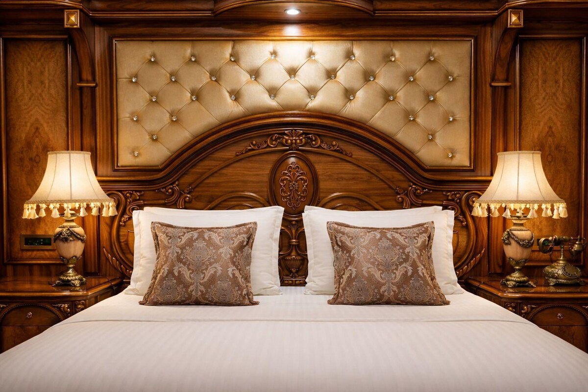 A luxurious bed with a tufted headboard, two matching lamps, and ornate bedside tables.