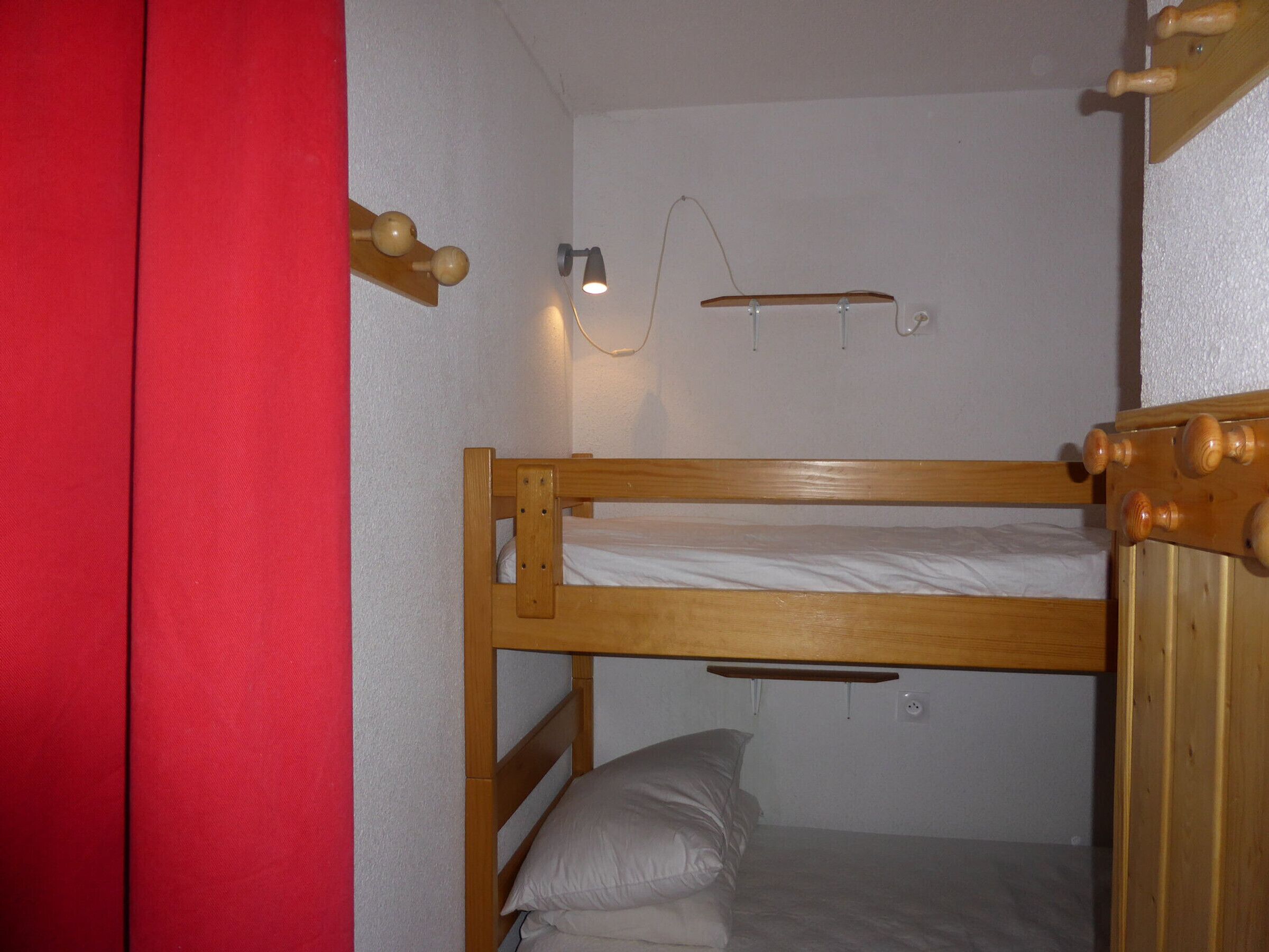 A bunk bed with a wooden frame and a single bed below. There is a wall-mounted light fixture above the bed.