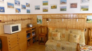 A cozy room with wooden paneling, a sofa with a patterned cover, a microwave, and shelves with various items. - Cozy 2-room apartment for 4 pers with pets and parking (Les Contamines-Montjoie)