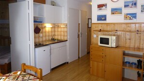A compact kitchen with white cabinets, a wooden countertop, a microwave, and a sink. There are wooden shelves above the counter and a clock on the wall. - Cozy 2-room apartment for 4 pers with pets and parking (Les Contamines-Montjoie)