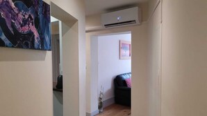 Un pasillo estrecho con piso de madera, un equipo de aire acondicionado en la pared y un cuadro en la pared contigua.