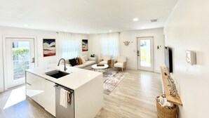 Cozinha moderna com ilha central, área de jantar com mesa redonda e sala de estar com sofá e cadeiras.