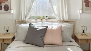 Quarto com uma cama grande, luminária pendente, janela com cortinas e obras de arte nas paredes.