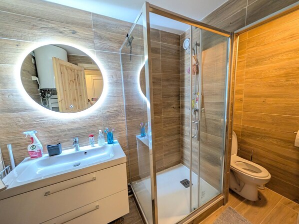 A modern bathroom with a glass-enclosed shower, a white sink with toiletries, and a large mirror.