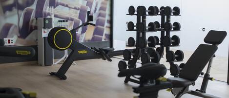 Una palestra con attrezzature per esercizi, una rastrelliera per manubri a parete e una finestra con vista su edifici e alberi.