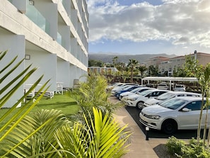 A hotel parking lot with multiple white cars, a covered parking area, and a building with a modern design. - MYND Adeje (Adeje)