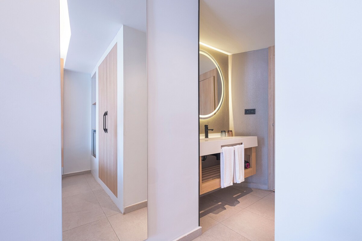 Un baño moderno con tocador, espejo redondo y perchero.