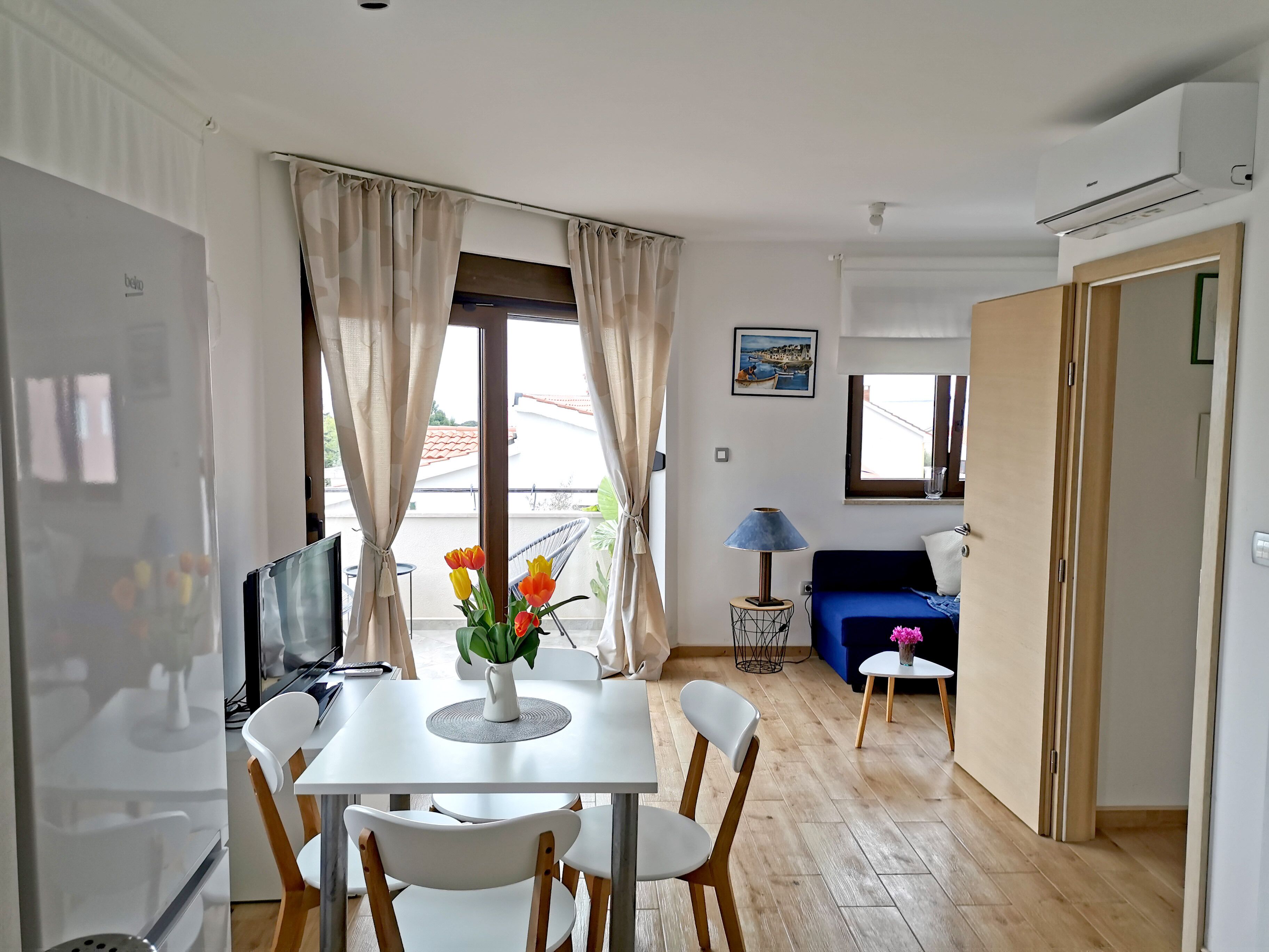 A modern living room with a dining area, a TV, and a view of the outside.