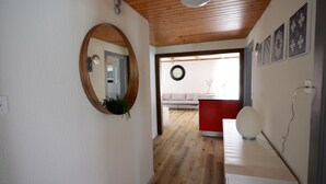 En hall med ett träpanelat tak, en rund spegel, en röd disk och en vit soffa i bakgrunden.