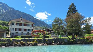 Ett hotell vid sjön med en stenmur, kristallklart vatten och utsikt över bergen.