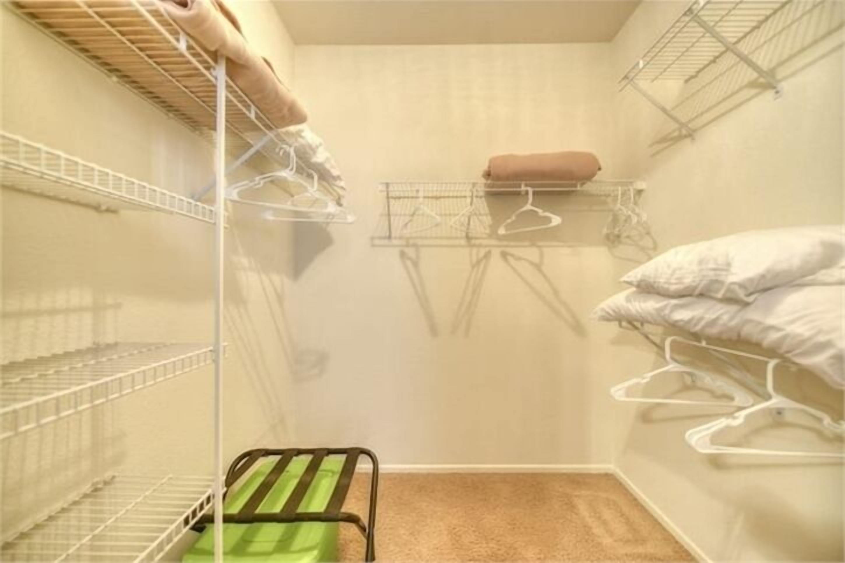 A small, compact closet with metal shelves and hangers, a green chair, and a beige carpet.