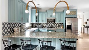 Una cocina con armarios verde azulado, encimera de granito y cuatro taburetes negros.