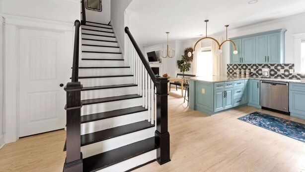 Una cocina con gabinetes azul claro, un salpicadero blanco y negro estampado, y un tapete azul con motivos florales.