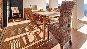 Un comedor con una mesa y sillas de madera, una silla de mimbre y vistas al exterior.