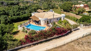 Ein großes Haus mit Swimmingpool, umgeben von üppiger Vegetation und einer hügeligen Landschaft.