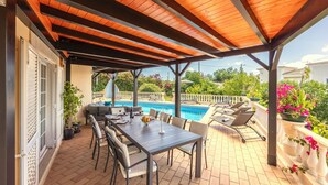 Eine überdachte Terrasse mit Pool, Sitzgelegenheiten im Freien und Blick auf den Poolbereich.