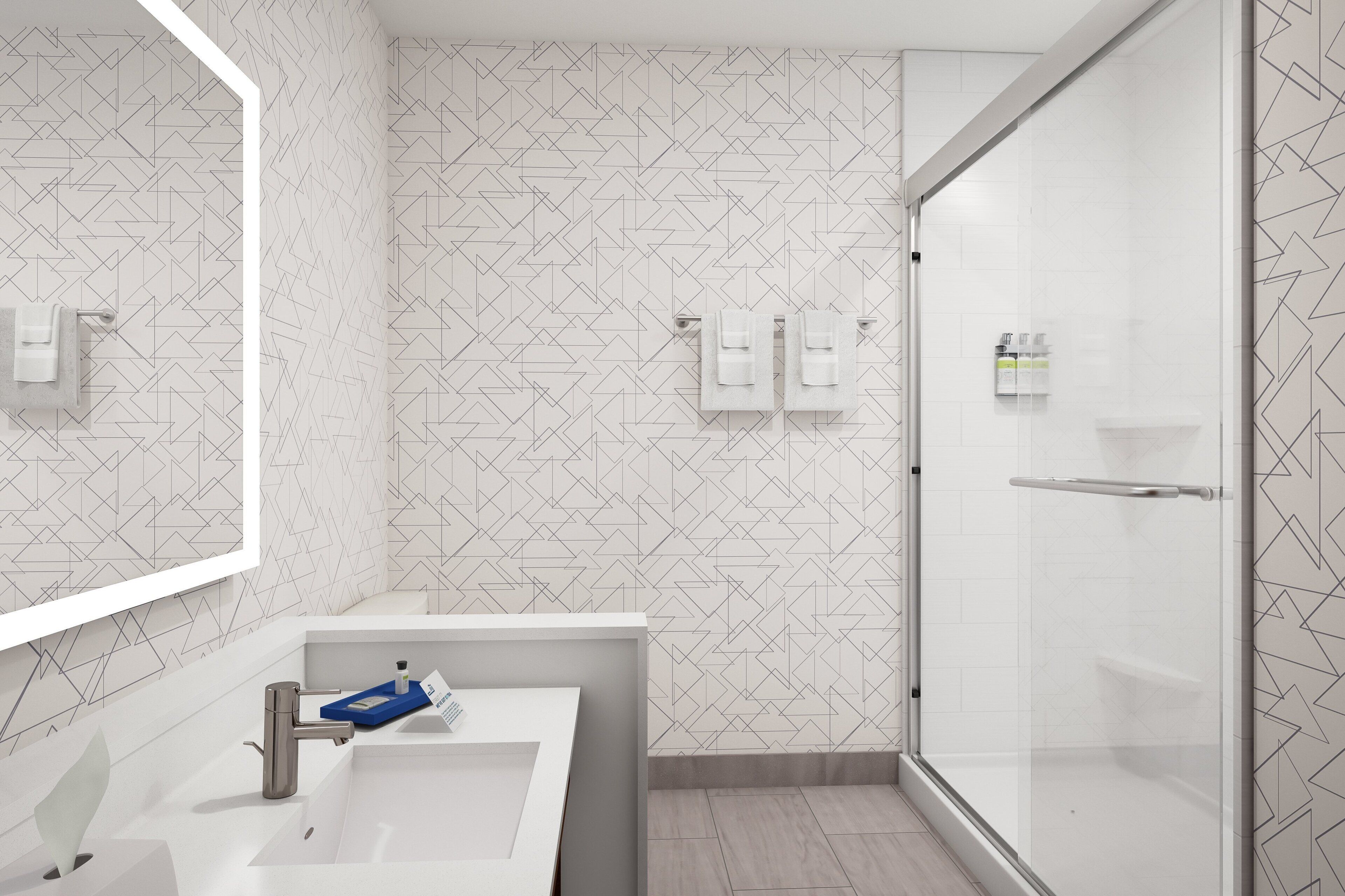 Une salle de bain moderne avec un mur orné d’un motif géométrique, un lavabo blanc avec un porte-savon bleu et une cabine de douche en verre.