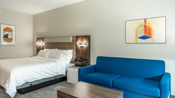 A hotel room with a bed, a blue sofa, a wooden coffee table, and a painting on the wall.