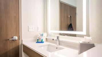 A modern bathroom with a white sink, a large mirror, and a wooden door.