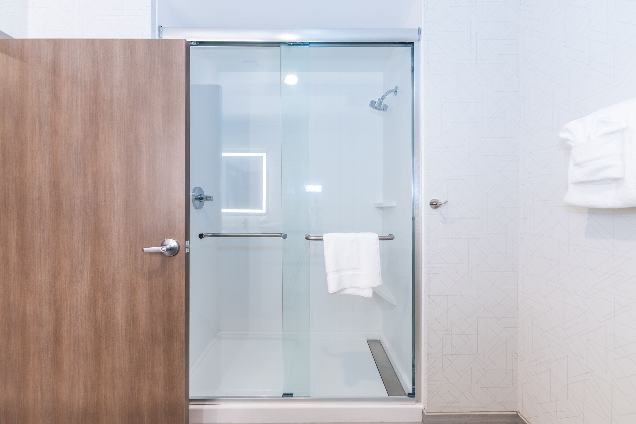 Un baño moderno con cabina de ducha de vidrio, una puerta de madera y un perchero para toallas.