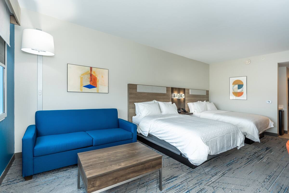 Ett hotellrum med en blå soffa, ett träbord, en stor säng med vita sängkläder och två sängbord.