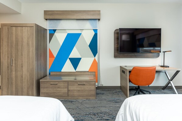 A hotel room with two beds, a desk with an orange chair, a TV, and a wardrobe.