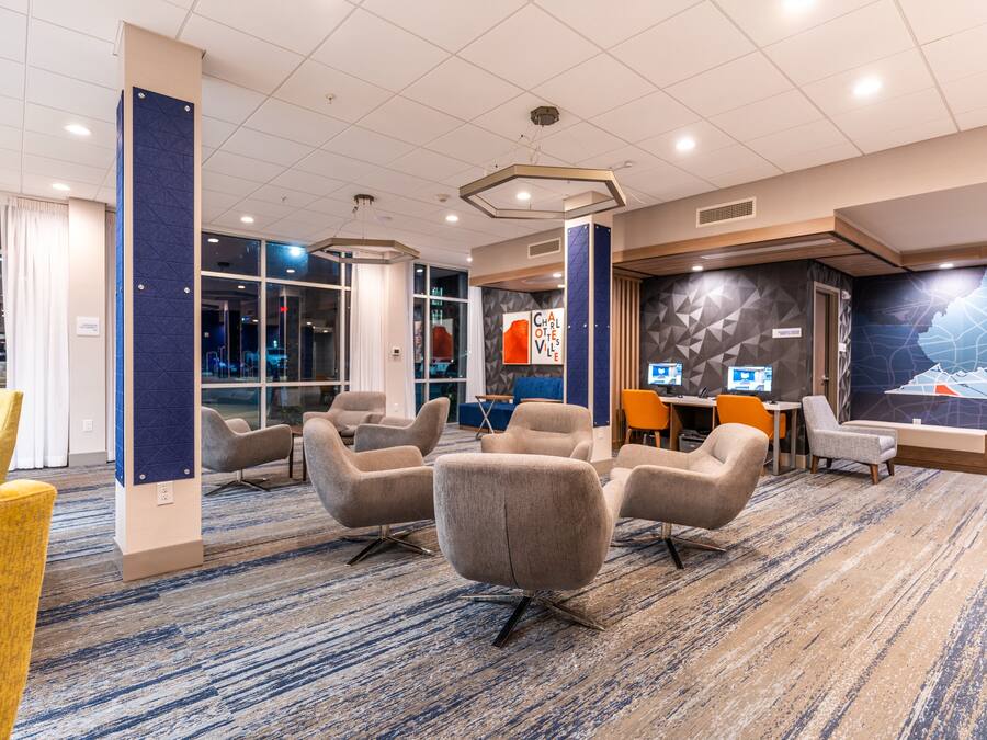A modern hotel lobby with a carpeted floor, multiple seating areas, and a large wall mural.